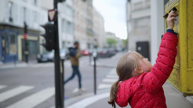Adorable preschooler girl putting letter in yellow post box on a street of Paris