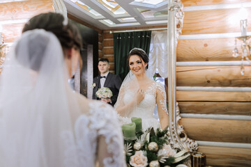 Elegant brunette bride poses in a white dress near the mirror. Portrait of the bride, wedding...