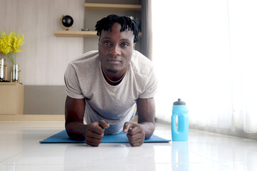 Young handsome African sport man doing a plank exercise at home. Male athletic in workout clothes training body and doing planking exercises.