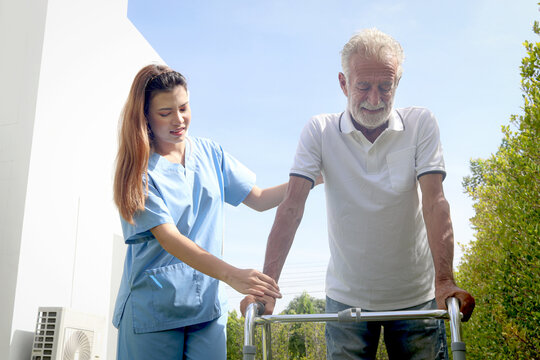 Female nurse or doctor help elderly patient lean to walk with orthopedic walker at outside, patient practice walking in garden with physiotherapist, nursing senior people at home, medical health care.