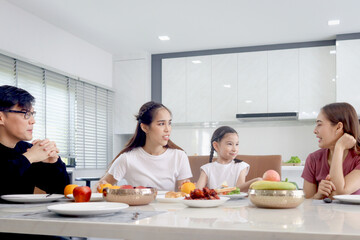 Happy family having meal in dining room. Parents, daughter and aunt sitting around dining table and having fun during breakfast. Cheerful family mother father and kid enjoy eating food together.