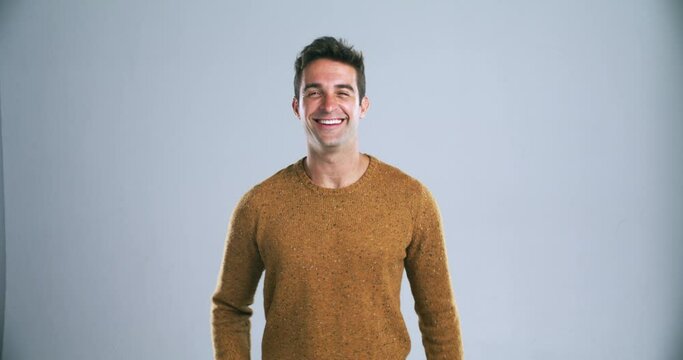 Young happy man, pointing and calling you in confidence isolated against a gray studio background. Portrait of handsome or attractive male person or model with finger or wink for choice on mockup