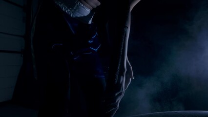 A woman in a semi-dark room rubs chalk on her hands before a hard workout and then picks up a hammer