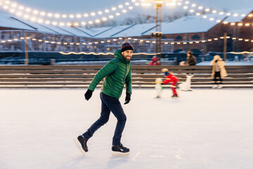 Obraz premium Man ice-skating joyfully in an outdoor rink with festive lights at twilight