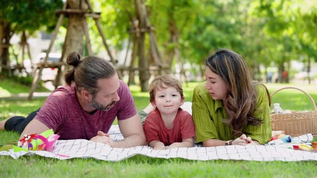 Happiness of Caucasian family during vacation father mother and son Lay out on grass while having picnic at park. To rest after tiring job. Everyone  lying face down on sheets that had been laid out.