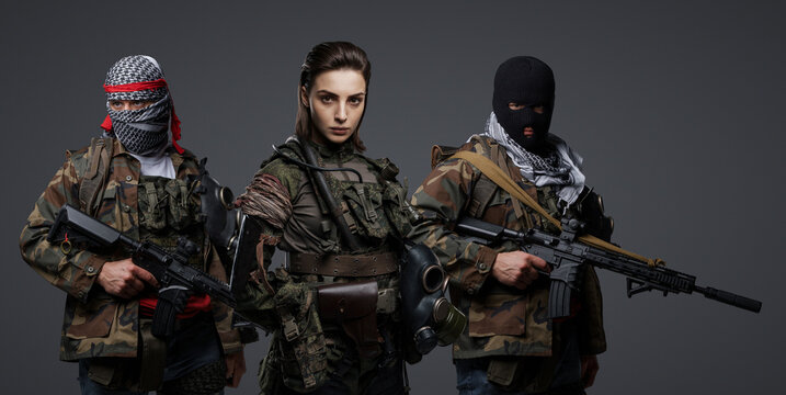 Group of three Middle Eastern militants dressed in camouflage uniforms, keffiyehs, and balaclavas posing against a gray background