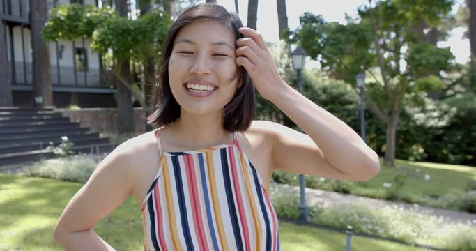 Happy asian woman with dark straight hair standing and smiling in sunny garden, slow motion
