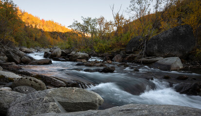 River flows in the vast landscape of Swedish Lapland on an autumn evening with surrounding autumn colors