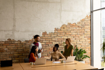 Fototapeta na wymiar Young multiethnic startup team working by the brick wall in the industrial style office