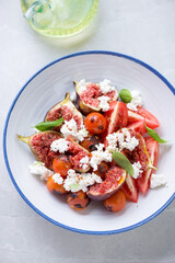Salad with fresh figs, roasted cherry tomatoes, goat cheese and green basil, vertical shot on a light-grey granite background, elevated view