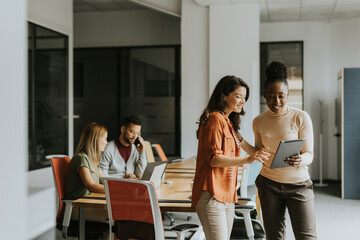 Two young business women with digital tablet in the office in front of their team