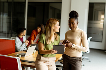 Two young business women with digital tablet in the office in front of their team