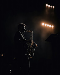 man playing a saxophone on stage at night, a backlight illuminates the silhouette of the musician