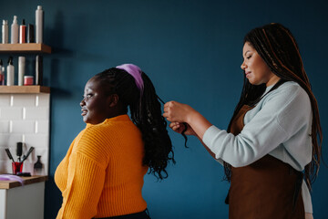 Confident African hairdresser braiding hair to a smiling female customer in hair salon