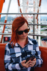 A woman is bored, she is not having fun on a stupid Ferris wheel attraction. Looking at smartphone....