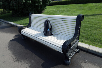 a small black backpack with a bottle of water lies on a white park bench