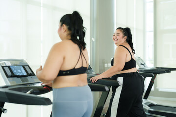 overweight two Asian women wearing exercise clothes, starting exercise, running on treadmill in fitness center, running at level that should run burn body tighten figure better.