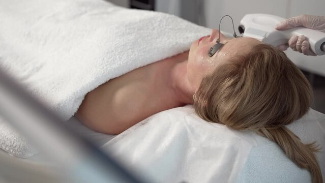 The therapist performs cosmetic plasma lifting using a high-intensity focal ultrasound machine. Anti-aging treatment and plastic surgery concept. Happy woman receiving cosmetic treatments. HIFU treatm