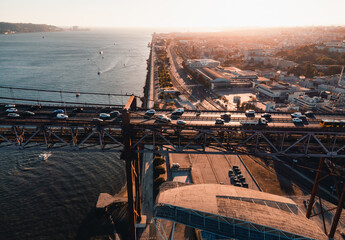 Aerial horizontal photo of streets and buildings of Lisbon on sunset. The Bridge of 25 april in Libson with harbor and Tagus river from above on golden hour - taken by drone.