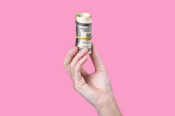 A hand holding a roll of money isolated on pink