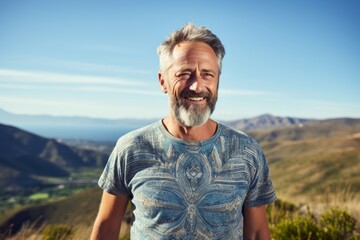 Portrait of a happy man in his 50s donning a trendy cropped top against a panoramic mountain vista....