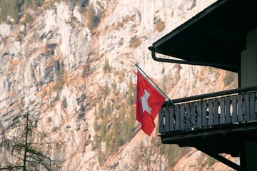 The Switzerland flag with a white cross on a red background waves on the house, offering a scenic attraction of the Grindelwald village and the mountains. Peaceful view of Grindelwald in the Alps.