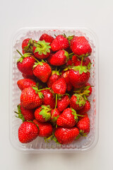 Fresh juicy strawberries in a transparent plastic container on the table.