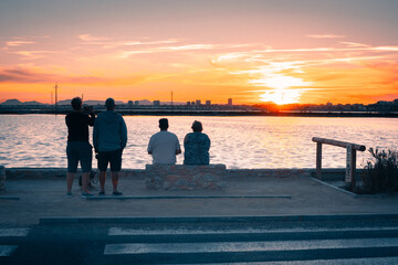 Personas junto al  mar contemplando el atardecer cuando el Sol esta apunto de perderse en el horizonte