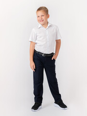 Beautiful smile. A cute 10-year-old blond schoolboy stands in a classic white shirt and dark trousers with a belt on a white background. Hand in my pocket. A glance to the side.