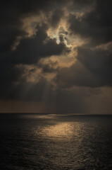 Fototapeta na wymiar Sun behind the clouds with rays falling on the sea