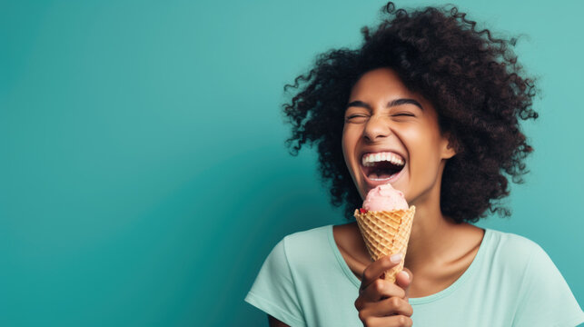 A woman wearing a big smile as she enjoys a waffle cone filled with colorful ice cream on a mint blue background, closeup. Copy space.