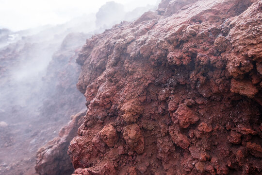 Close up of red lava rock on Mount Etna crater, Sicily island in Italy. Warm volcanic lava stone and smoke from crater of active volcano
