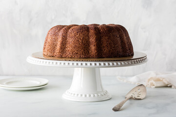A plain chocolate bundt cake on a pedestal stand against a light background.