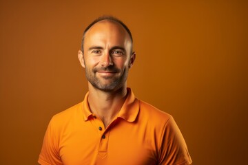 Obraz premium Portrait of a grinning man in his 30s wearing a breathable golf polo against a soft orange background. AI Generation