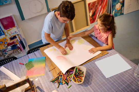 Top view of creative kids during an art class in a daycare center or elementary school classroom drawing