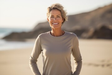 Portrait of a merry woman in her 50s sporting a long-sleeved thermal undershirt against a sandy...