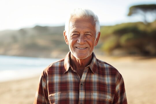 Portrait of a smiling man in his 80s dressed in a relaxed flannel shirt against a sandy beach background. AI Generation