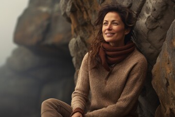 Portrait of a cheerful woman in her 40s dressed in a warm wool sweater against a rocky cliff...
