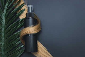 Blond shiny hair wave, Hair care spray and tropical leave on black background. Hair tools, beauty...
