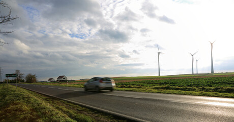 Samochód osobowy (poruszony) na drodze, turbiny wiatrowe w tle.