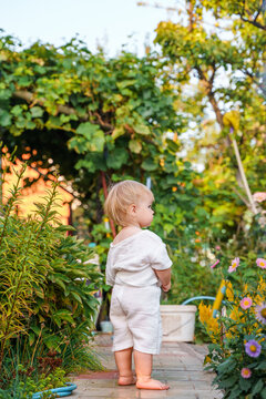 Little child baby in a muslin white suit in the garden at the dacha in summer, happy active summer