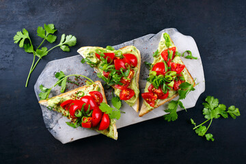 Traditionelles Toast Dreieck Sandwich mit Tomaten, Avocado Aufstrich und Kräuter serviert als Draufsicht auf einem grauen Design Tablett 