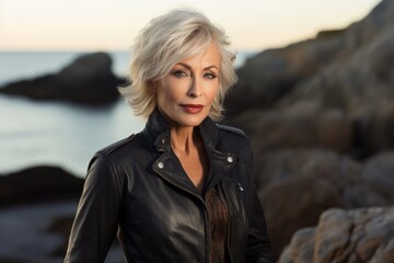 Portrait of a glad woman in her 60s sporting a stylish leather blazer against a rocky shoreline background. AI Generation - Powered by Adobe