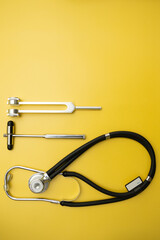 Stethoscope, Neurological Hammer and Tuning Fork C 128 on Yellow Background with Space for Text