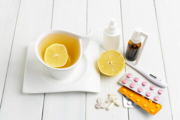 Tea cup with lemon, cold remedies, medicine, thermometer, capsules and pills in a blister pack on wooden table. Concept of home treatment flu and coronavirus