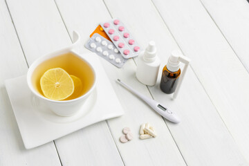 Tea cup with lemon, cold remedies, medicine, thermometer, capsules and pills in a blister pack on wooden table. Concept of home treatment flu and coronavirus