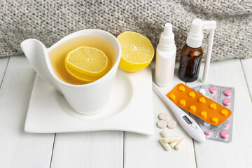 Tea cup with lemon, cold remedies, medicine, thermometer, capsules and pills in a blister pack on wooden table. Concept of home treatment flu and coronavirus