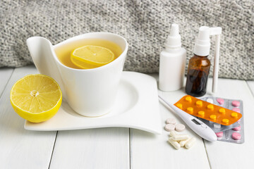 Tea cup with lemon, cold remedies, medicine, thermometer, capsules and pills in a blister pack on wooden table. Concept of home treatment flu and coronavirus