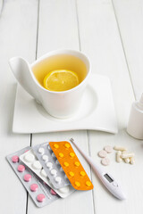 Tea cup with lemon, cold remedies, medicine, thermometer, capsules and pills in a blister pack on wooden table. Concept of home treatment flu and coronavirus