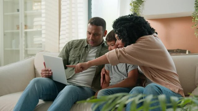 Happy multiracial family parents child kid using laptop computer on home couch excited African American mom dad Caucasian adopted little son boy celebrate achievement victory success winning at home